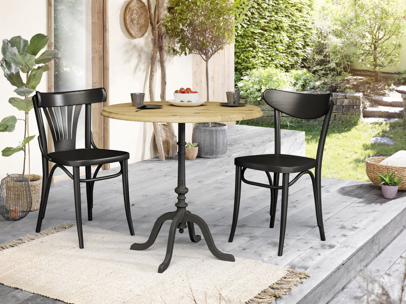 Runder Beizentisch mit hellem Massivholz und schwarzem Gusseisenfuss zwei schwarze Stühle auf Terrasse im Garten mit Sommerambiente